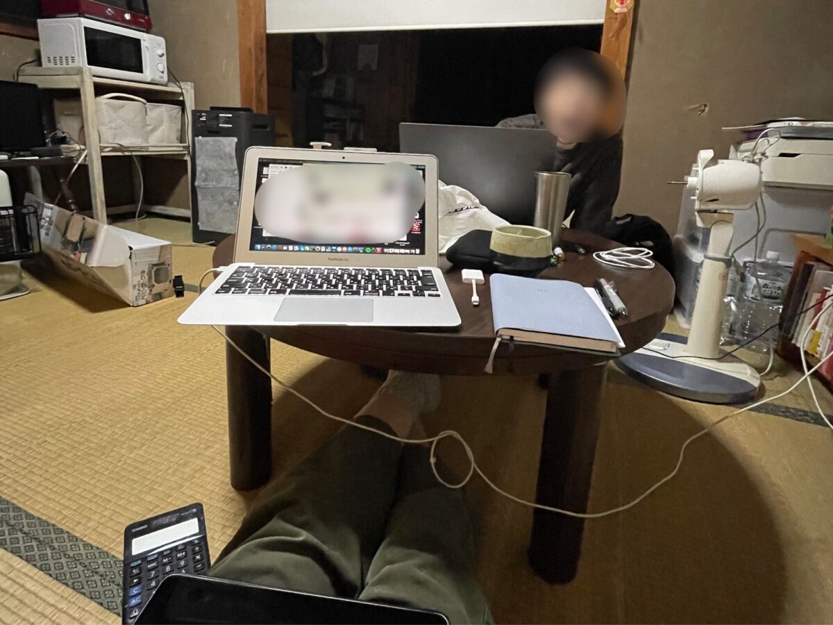 散らかった部屋で夫婦でPC作業する様子